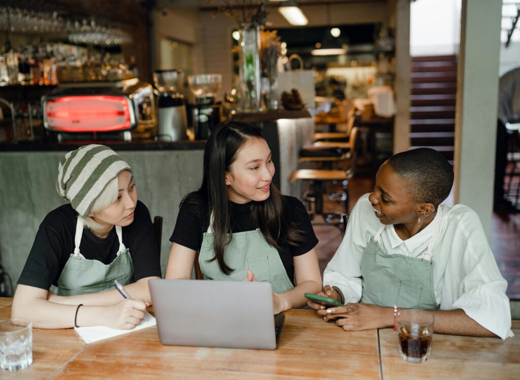 Equipo de hostelería reunido en un restaurante, revisando tareas de trabajo en un portátil.